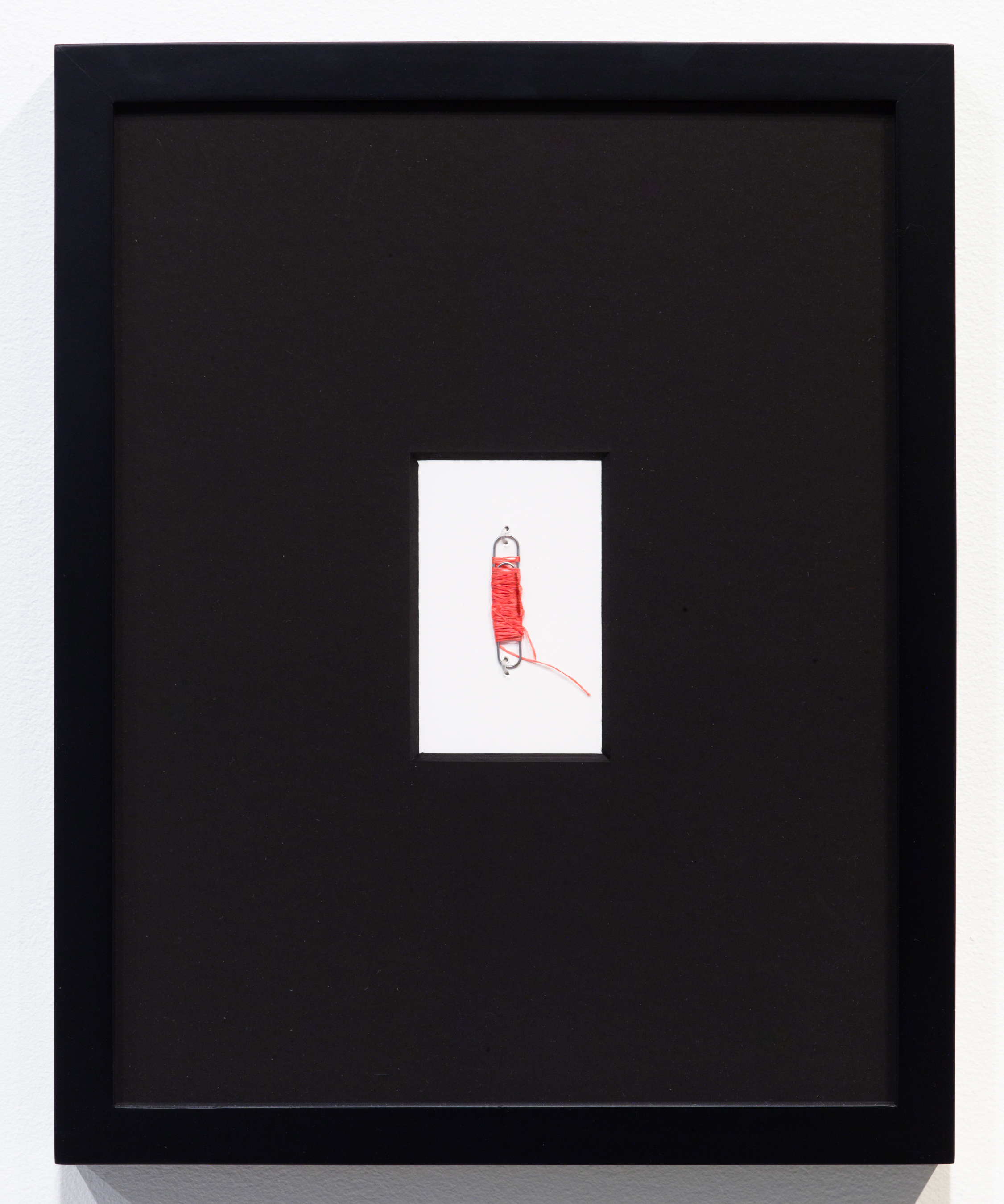 Red dental floss wrapped around a paperclip insdie a large black frame